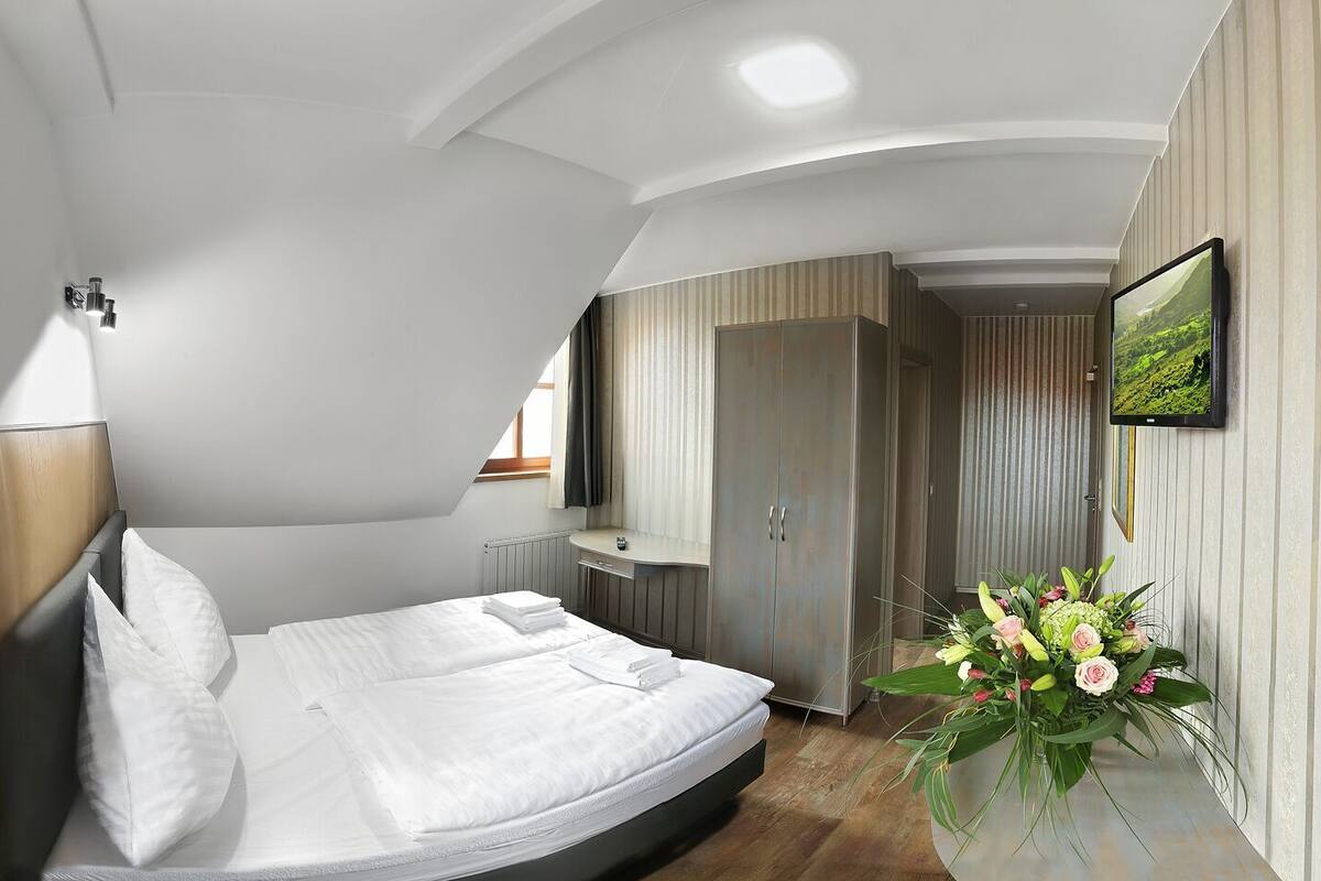 A modern bedroom with a bed, bedside table, wardrobe, and a decorative plant.