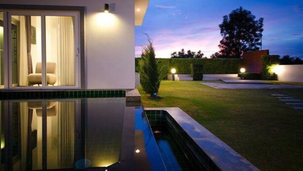 A modern house with a swimming pool, a glass door entrance, and a well-lit garden at dusk. - L.A. Pool Villa Huahin (Hua Hin)