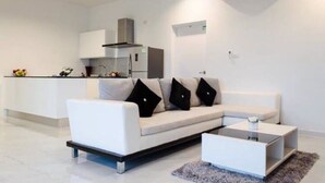 A modern living room with a white sofa, a coffee table, and a kitchen area in the background. - L.A. Pool Villa Huahin (Hua Hin)