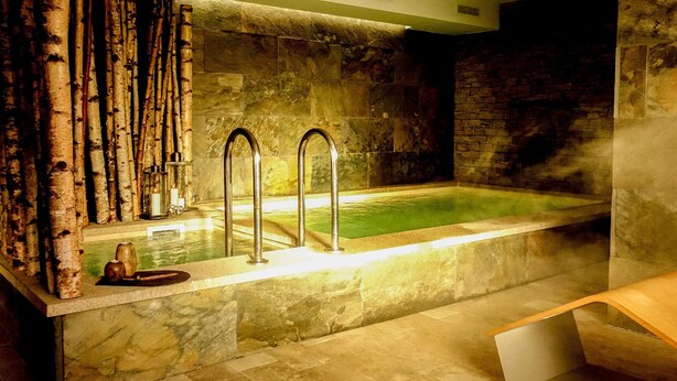 Un espace de détente avec un mur en pierre, un banc en bois et une baignoire.