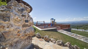 Un terrain de jeux équipé de balançoires et de structures d’escalade, avec en toile de fond des montagnes et un ciel dégagé.