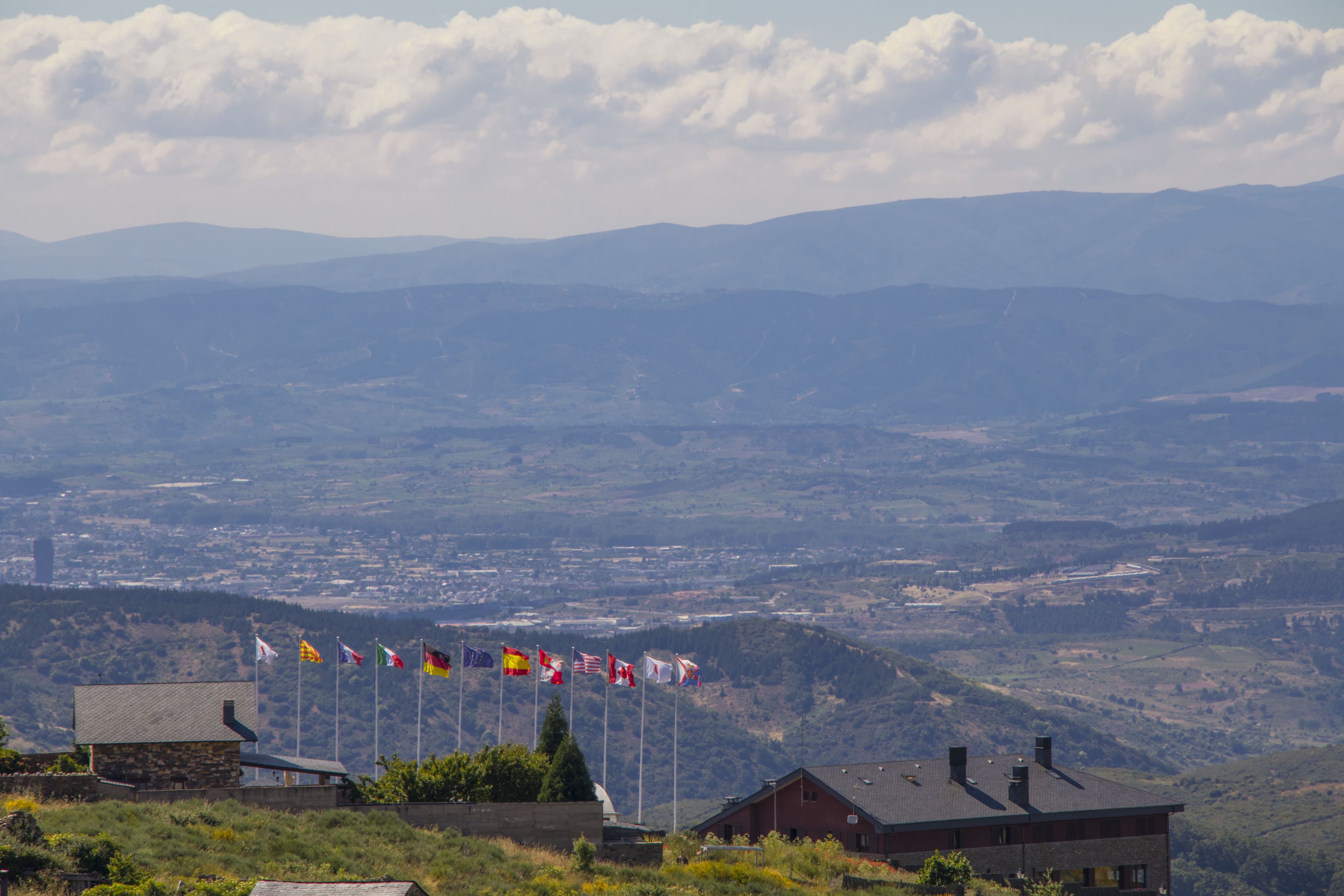 A view of a mountainous landscape with a building featuring multiple flags in the foreground.
