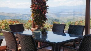 Un coin repas avec une table en verre et des chaises en osier, donnant sur un paysage montagneux.