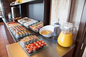 Una mesa de buffet con diversos alimentos y una jarra de jugo de naranja.