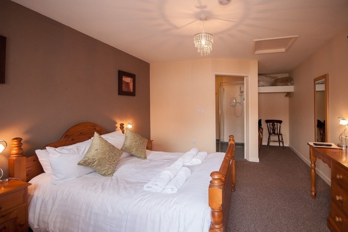A hotel room with a large bed, bedside lamps, a chandelier, a wooden dresser, and a small desk with a lamp.