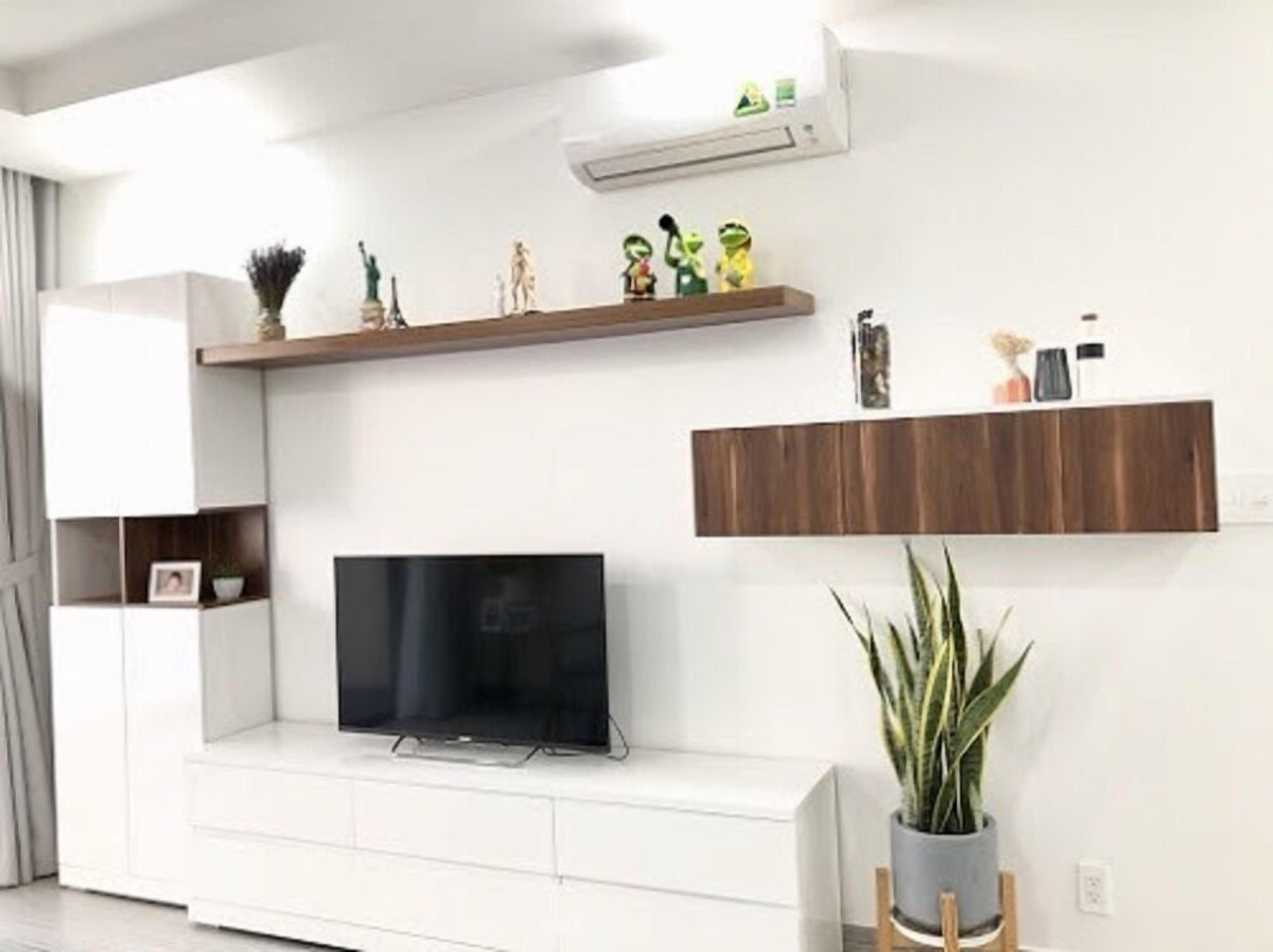 Una sala de estar moderna con un televisor de pantalla plana, muebles blancos y objetos decorativos en estanterías.