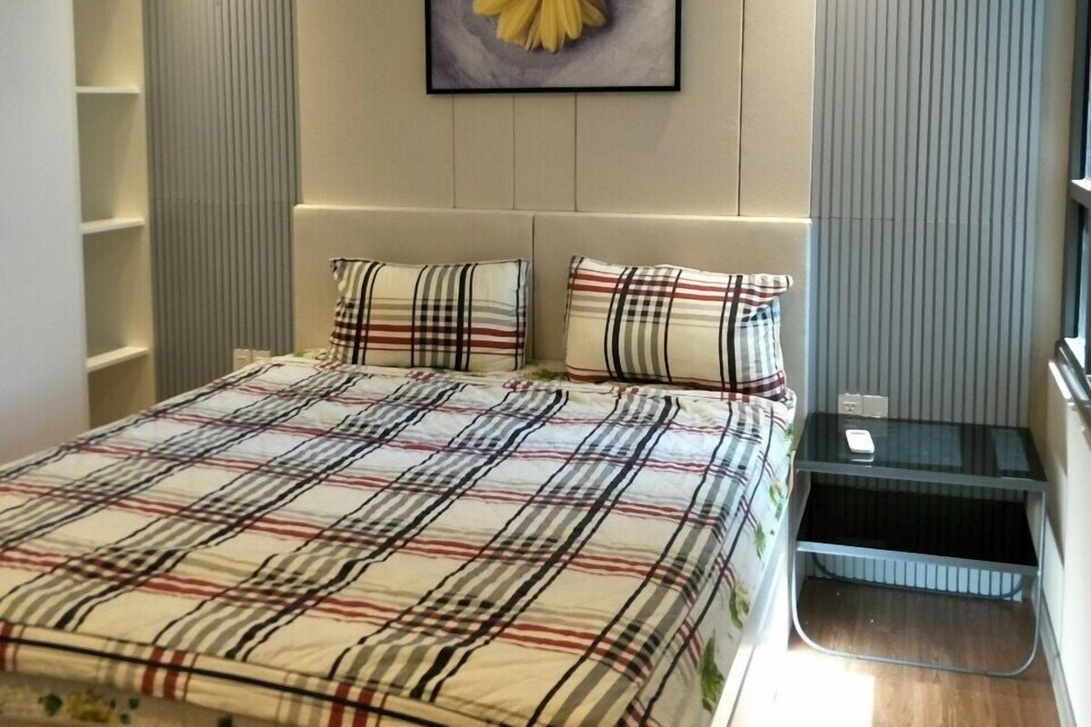 A modern bedroom with a large bed, a headboard with vertical lines, a bedside table, and a wall-mounted artwork of a flower.