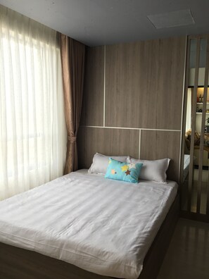 A modern bedroom with a large bed, light-colored bedding, a wooden headboard, and sheer curtains.