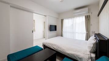Habitación de hotel con cama, televisión, escritorio y ventana con cortinas.
