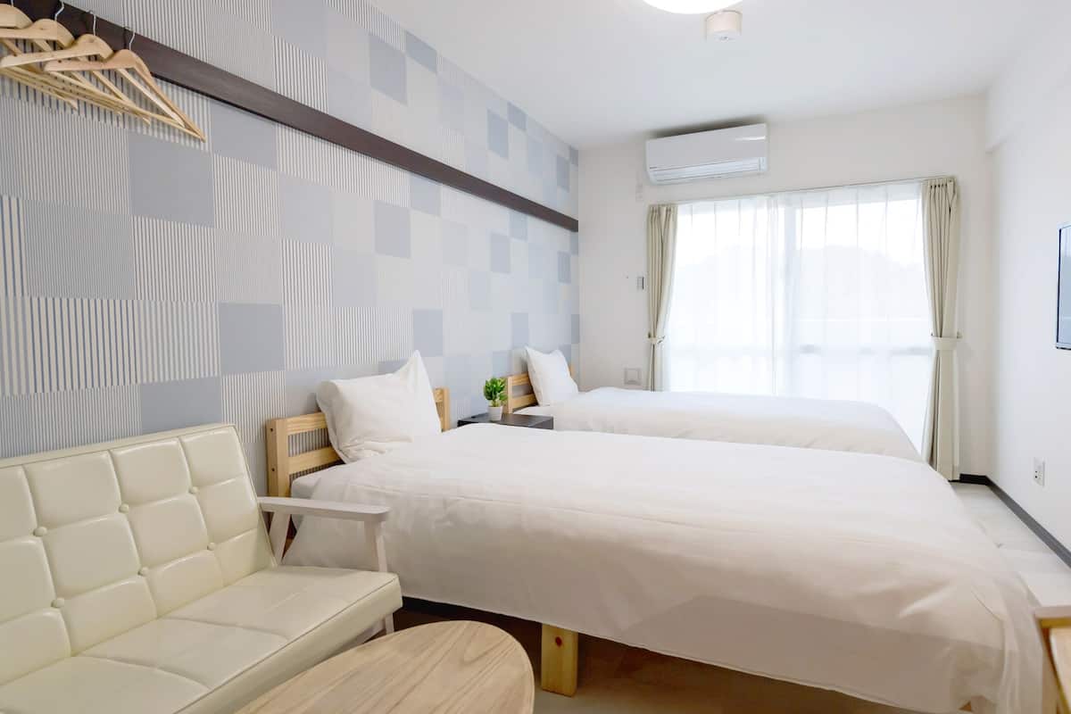 A hotel room with two beds, a sofa, a TV, and a window with curtains.
