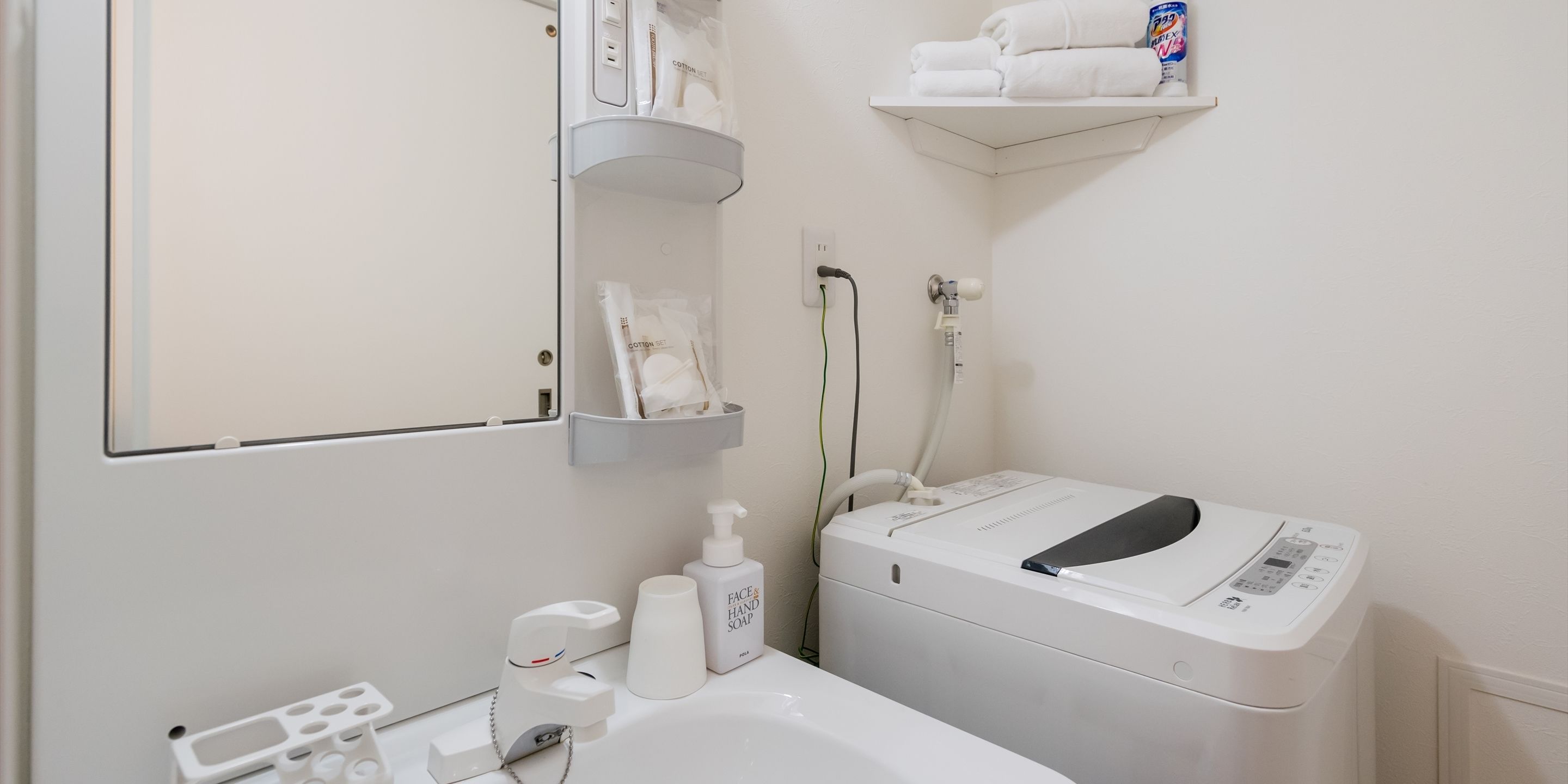 Un baño con lavamanos blanco, espejo, toallero, dispensador de jabón para manos y lavadora blanca.