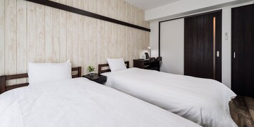 Habitación de hotel con dos camas, un escritorio con lámpara, una planta pequeña y un armario de madera oscura.