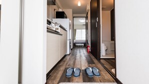A narrow hallway with a wooden floor, a white refrigerator, a microwave, and a bed in the background. - Hotel Tomas Nago (Nago)