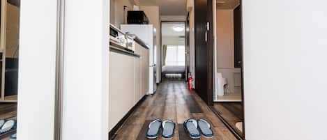 A narrow hallway with a wooden floor, a white refrigerator, a microwave, and a bed in the background.