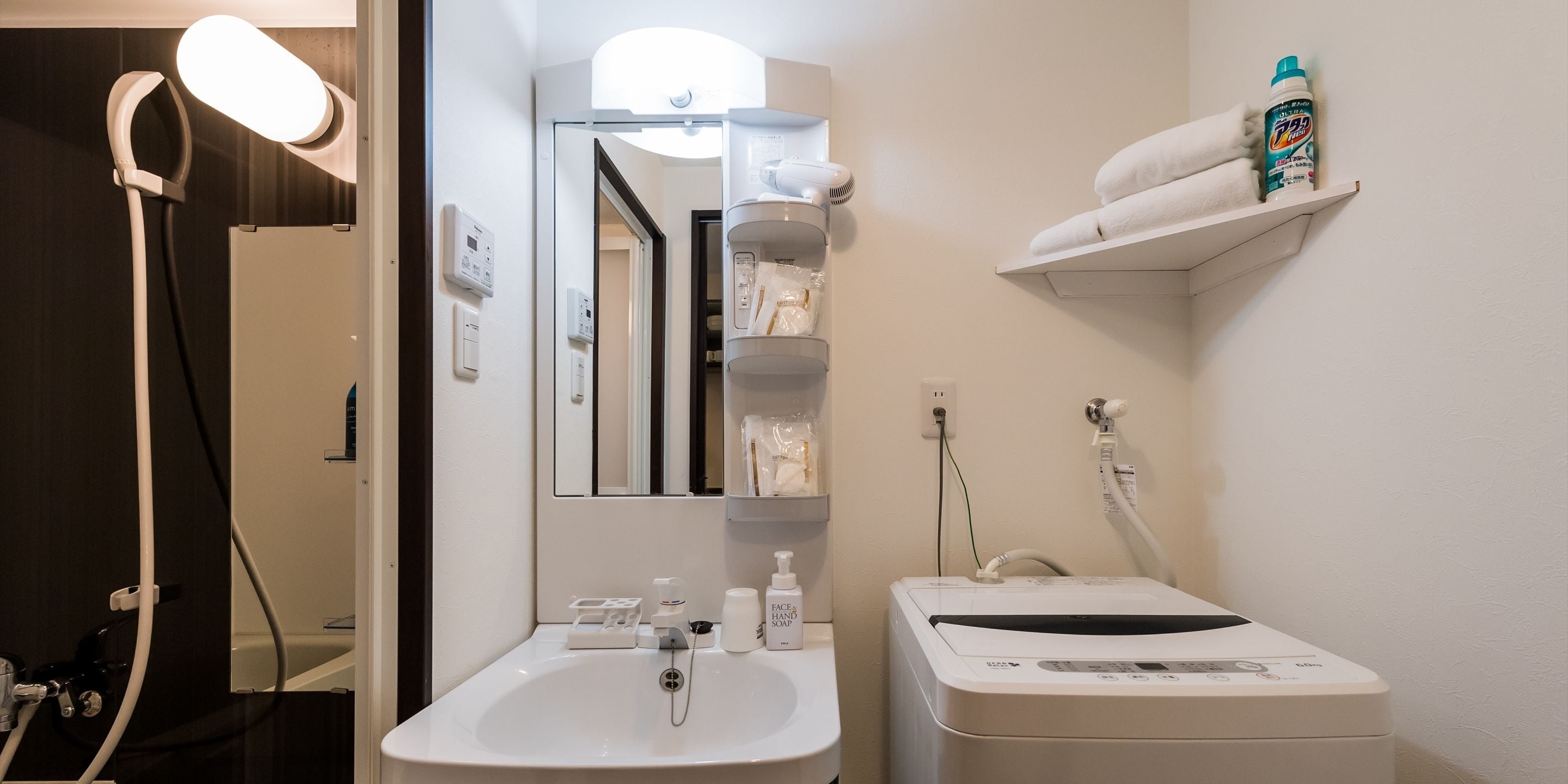 Een badkamer met een witte wastafel, spiegel en handdoekhouder. Op het aanrecht liggen een haardroger en een fles handzeep.