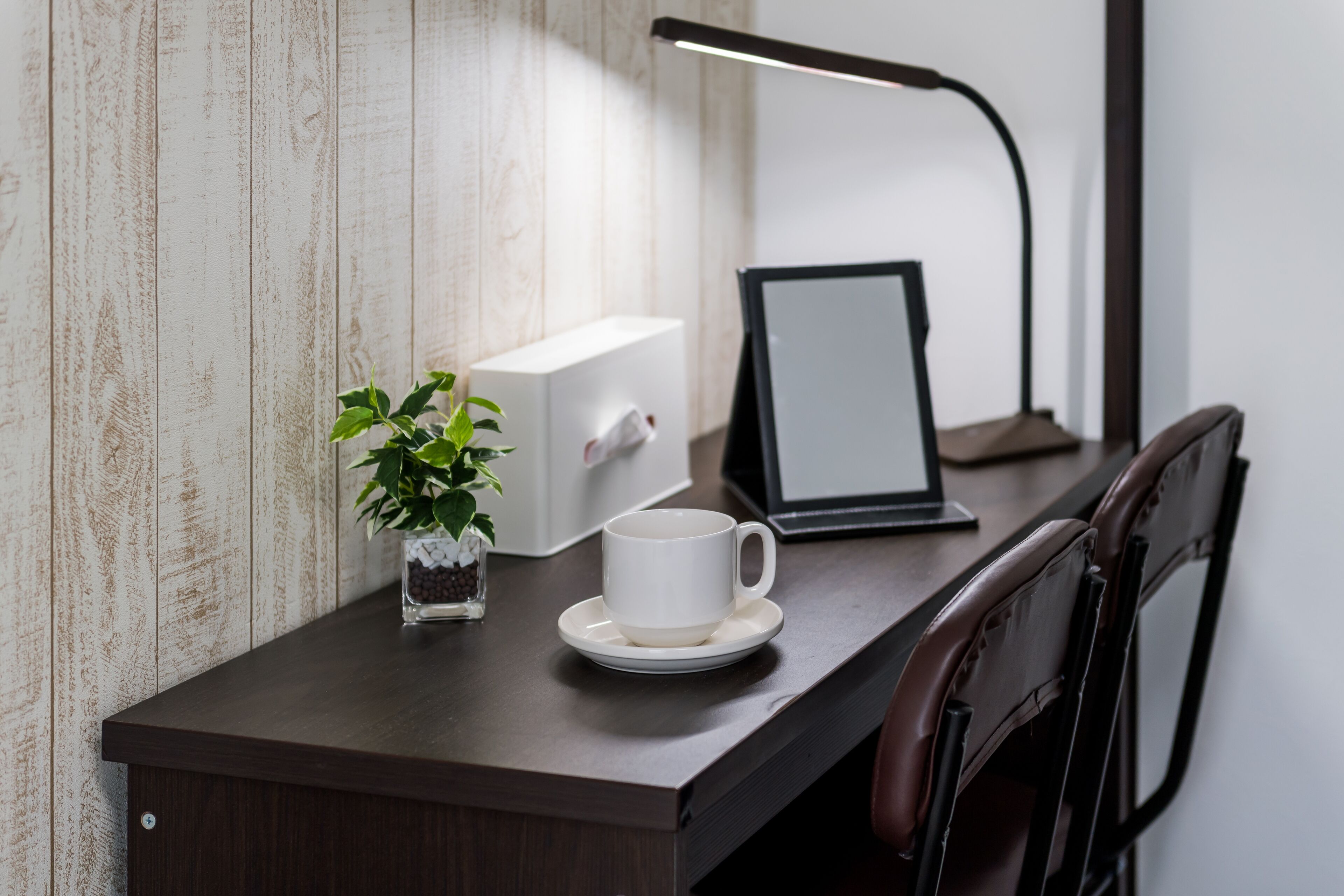 A wooden desk with a white mug, a small potted plant, a framed picture, and a desk lamp.