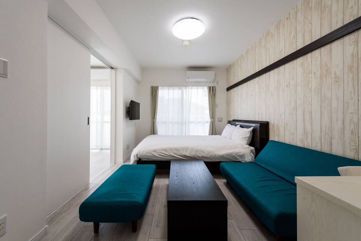A modern hotel room with a bed, teal sofa, bench, and a wooden accent wall.