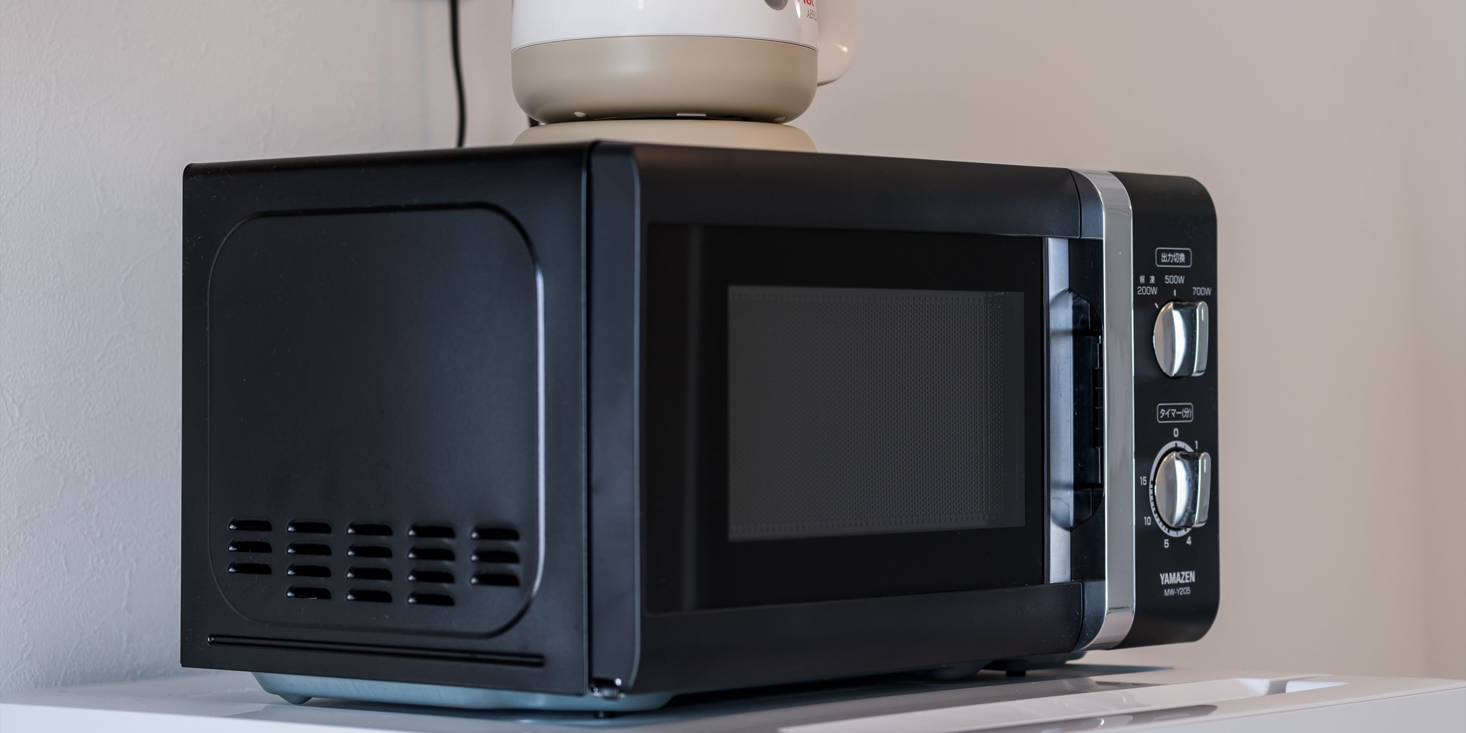 A black microwave oven with a control panel on the right side, placed on a white surface.