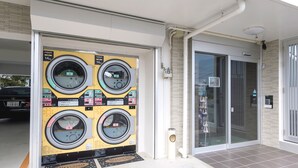 A laundromat with four washing machines, a glass door entrance, and a tiled floor. - Hotel Tomas Nago (Nago)