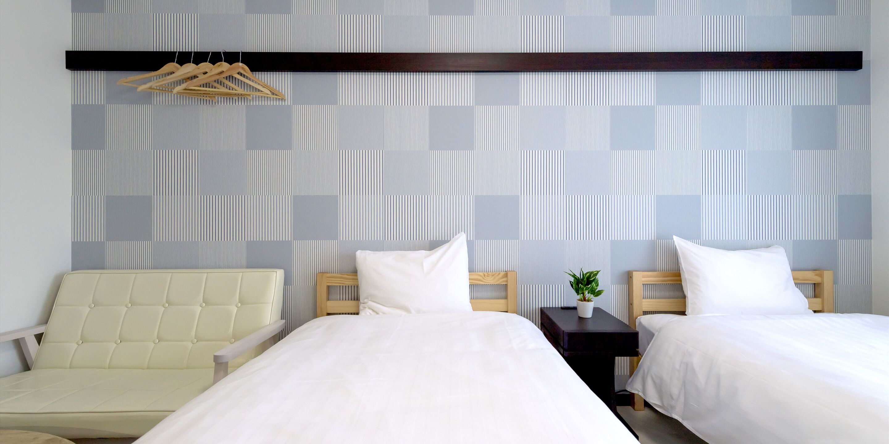 A hotel room with two beds, a chair, and a small table with a plant.