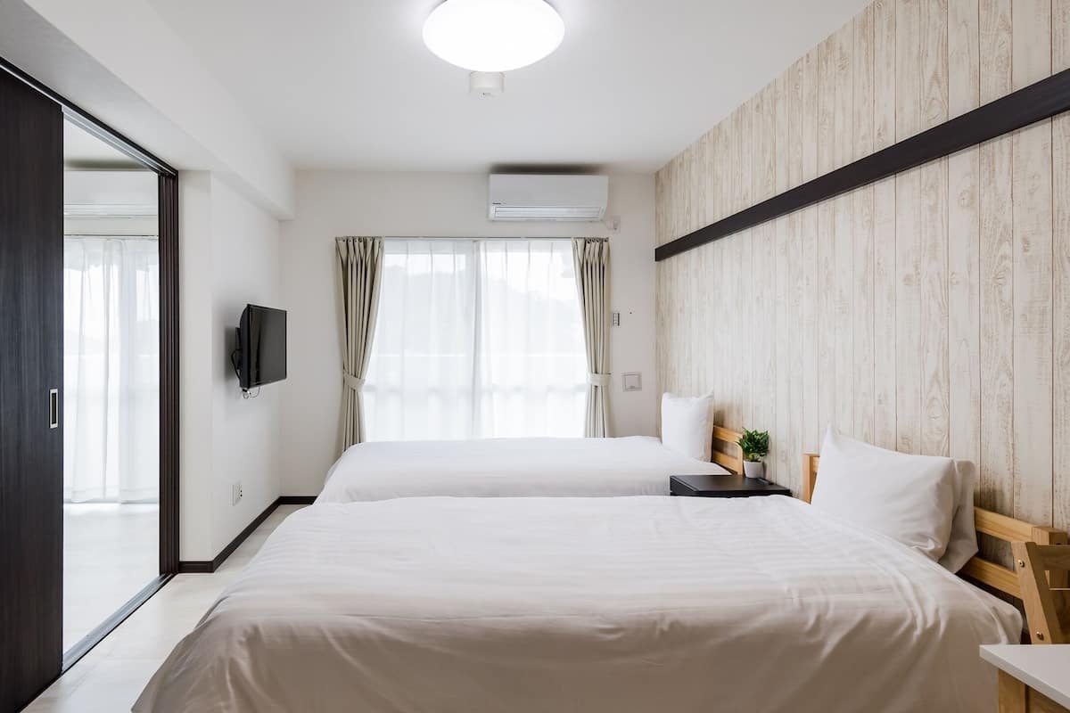 A hotel room with two beds, a TV, a plant, and a wooden wall.