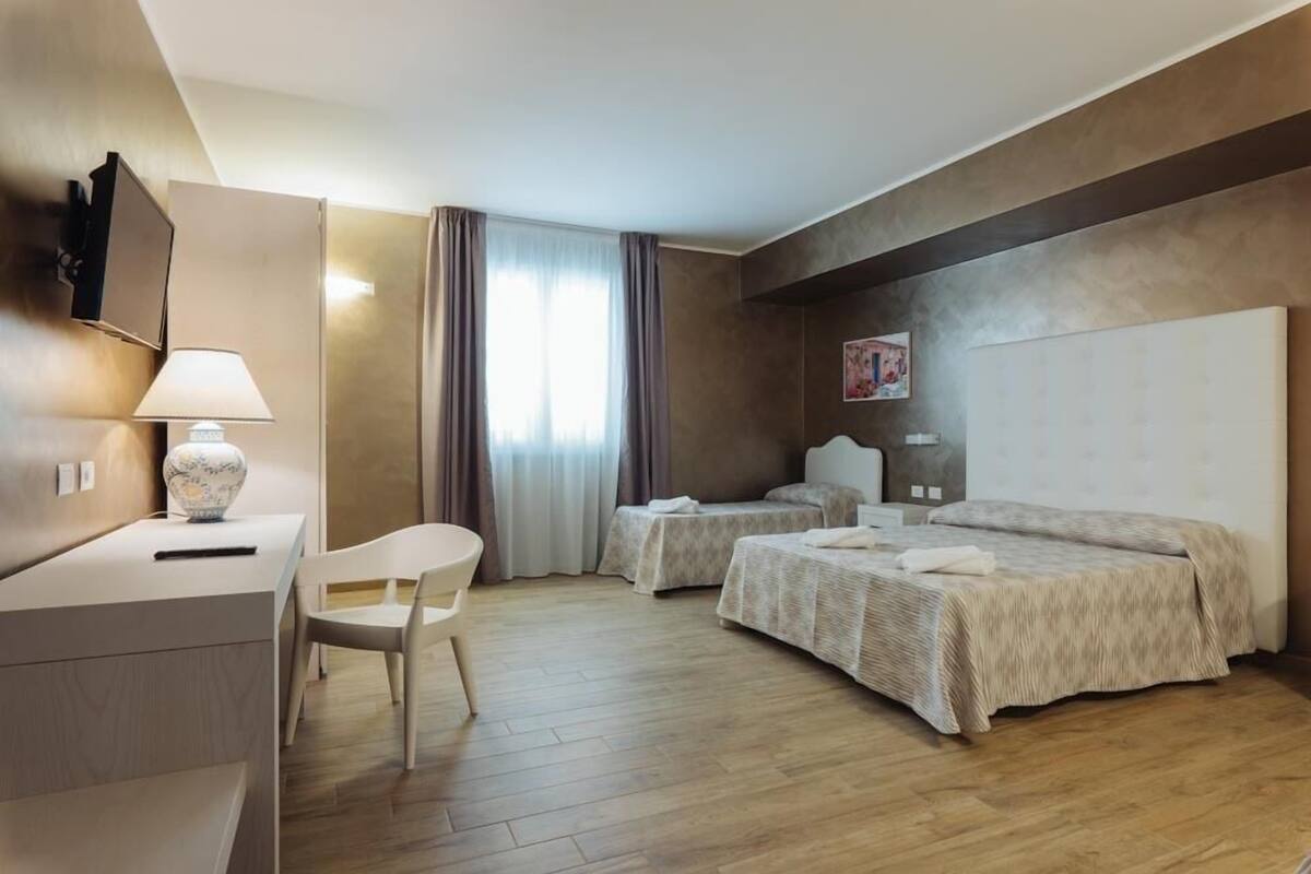 A hotel room with two beds, a desk, a chair, a lamp, and a painting on the wall.