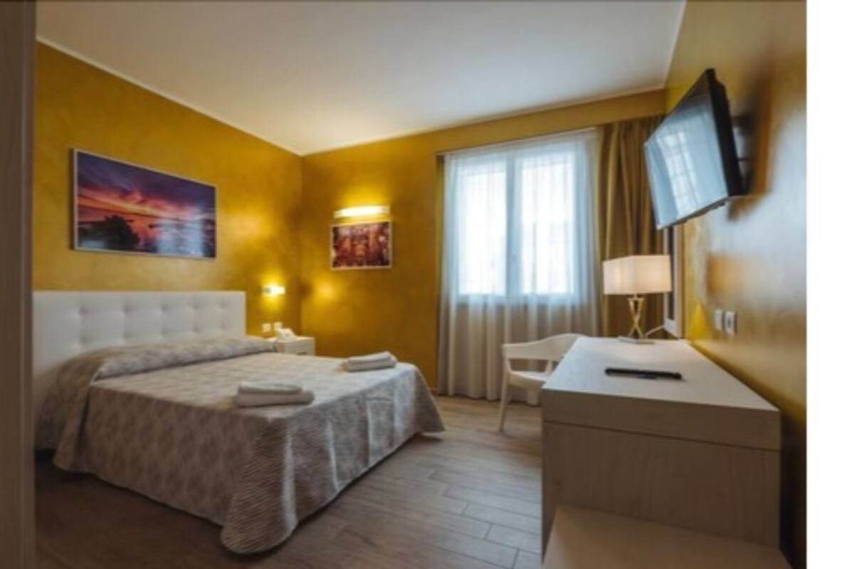 A hotel room with a bed, bedside table, lamp, and a painting on the wall.