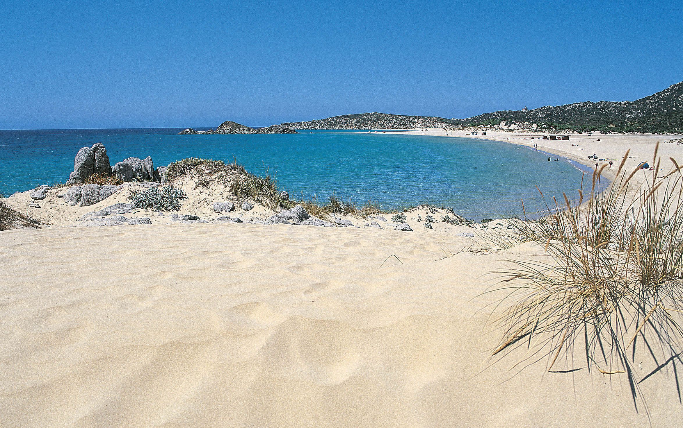 A beach with clear blue water, sandy shore, and rocky outcrops.