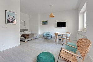 A modern, well-lit room with a bed, a dining table with chairs, a TV mounted on the wall, and a wicker chair. - Laguna Centrum Apartments (Sopot)