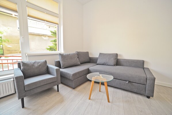Un salon moderne avec un canapé d’angle gris, un petit fauteuil et une table basse en verre.