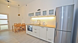 Uma cozinha moderna com armários brancos, uma geladeira de aço inoxidável, uma mesa de jantar de madeira com cadeiras e um forno embutido.