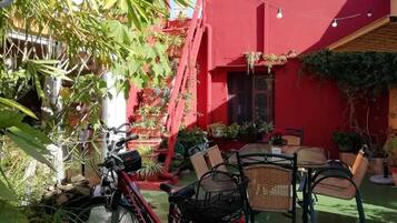 Un edificio rojo con techo verde, una bicicleta y mesas al aire libre.