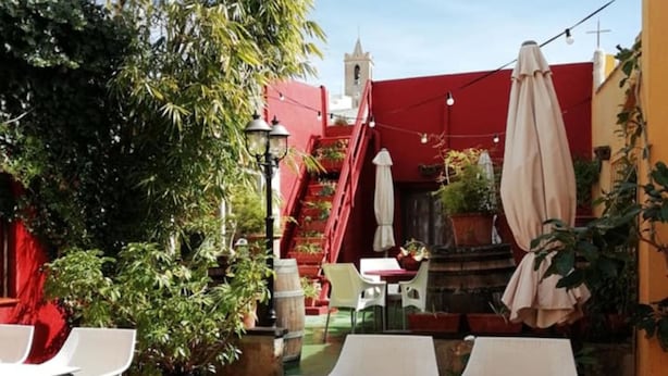 An outdoor patio with white tables and chairs, a red staircase, and a tower in the background. - Casa Antiquary (Benitachell)