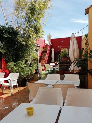 An outdoor patio with white tables and chairs, a red staircase, and a tower in the background. - Casa Antiquary (Benitachell)