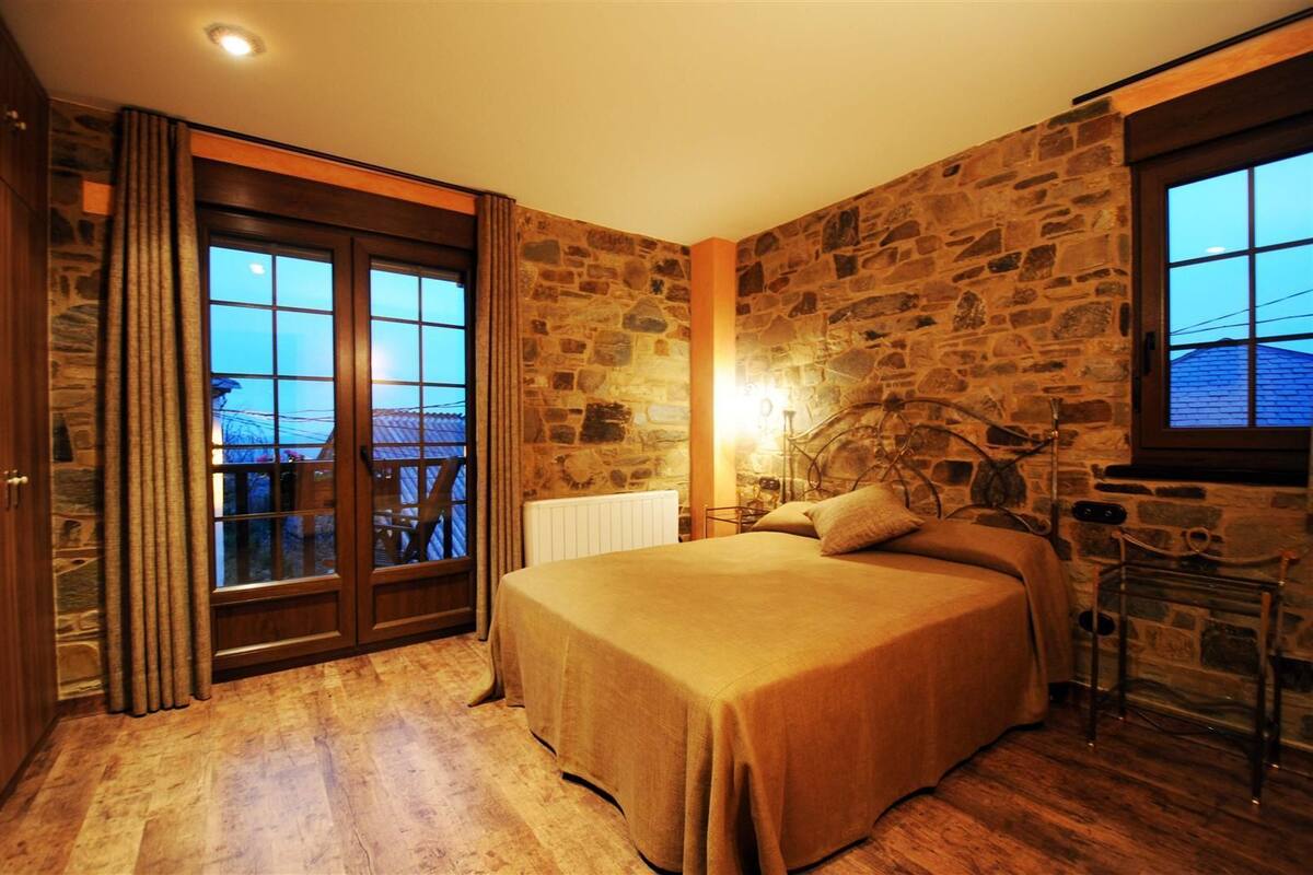 A bedroom with a stone wall, a bed, a window, and a view of the outside.