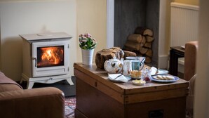 Uma sala de estar acolhedora com uma lareira a lenha, um baú de madeira e uma mesa posta com chá e biscoitos.