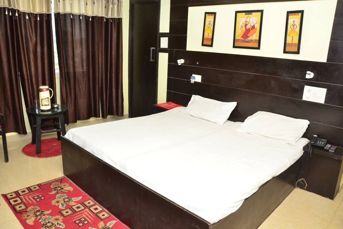 Habitación de hotel con una cama grande, una mesita de noche, un tapete rojo y una obra de arte en la pared.