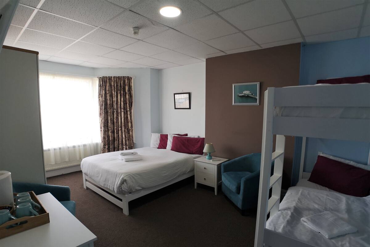 A hotel room with a single bed, a desk with a chair, a bunk bed, and a window with curtains.