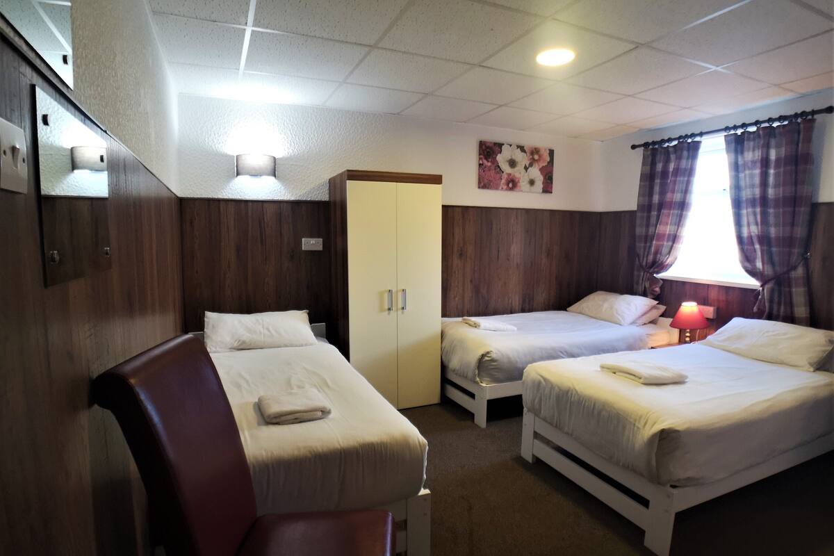 A hotel room with two single beds, a wooden wardrobe, a desk, and a chair.