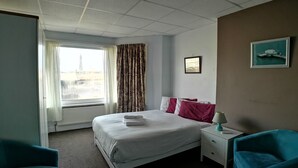 A hotel room with a bed, two pillows, a nightstand with a lamp, and a window with curtains. - The Hopton Hotel (Blackpool)