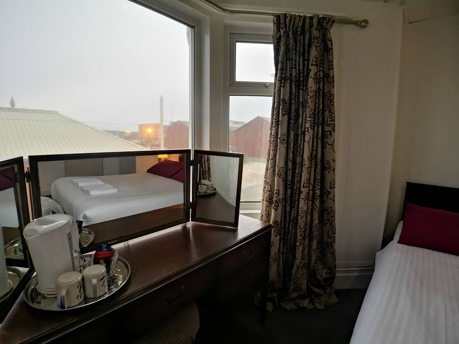 Habitación de hotel con cama, escritorio con una bandeja de objetos, ventana con cortinas y vista de edificios.