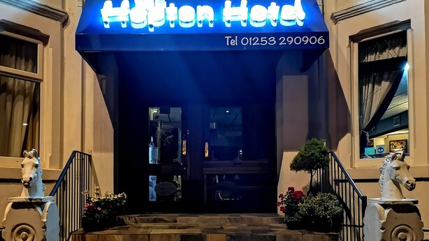 The entrance to the Hampton Hotel with a blue illuminated sign, stone steps, and two horse statues on either side. - The Hopton Hotel (Blackpool)