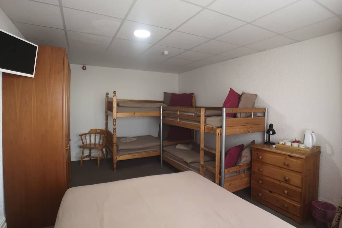 A bunk bed room with a TV, wooden dresser, and a desk with a lamp.