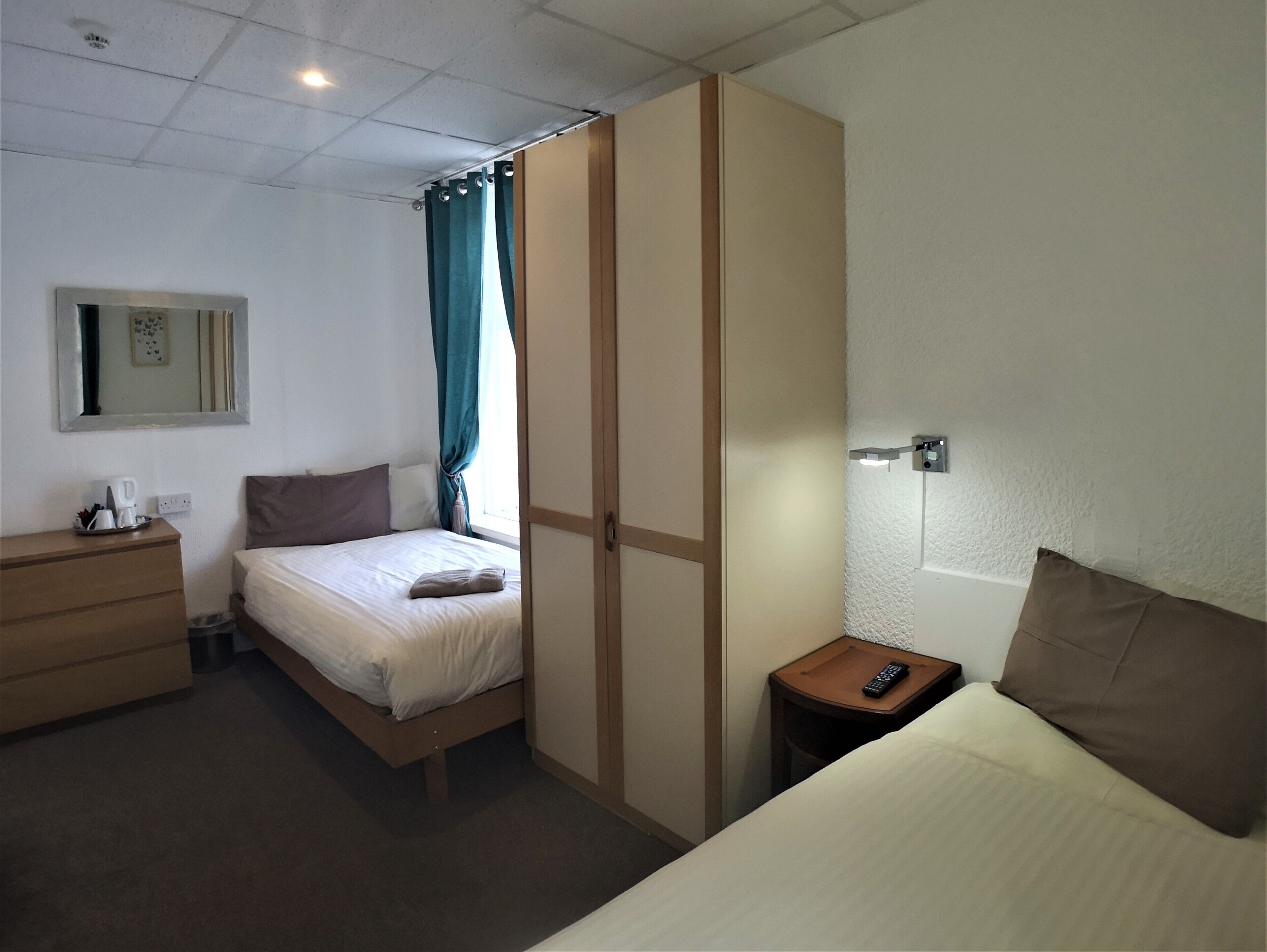 A hotel room with a bed, a dresser, a nightstand, a mirror, and a window with curtains.