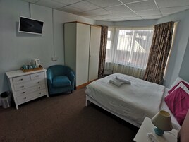 Hotelkamer met een bed, bureau, stoel, televisie en raam met gordijnen.