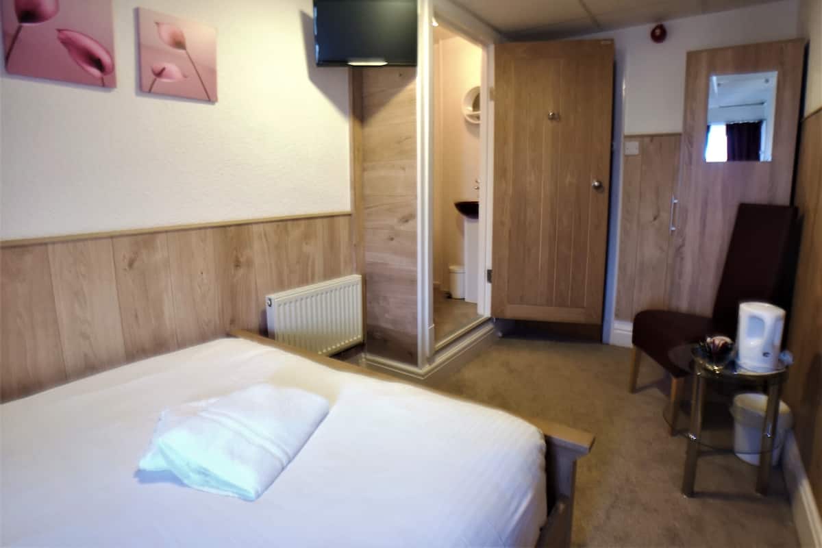 A hotel room with a bed, a chair, a small table with a cup, and a door leading to a bathroom.