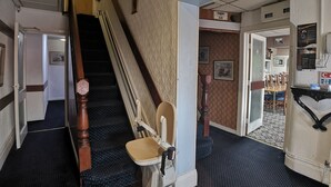 A hotel hallway with a staircase, a wheelchair, and a dining area. - The Hopton Hotel (Blackpool)