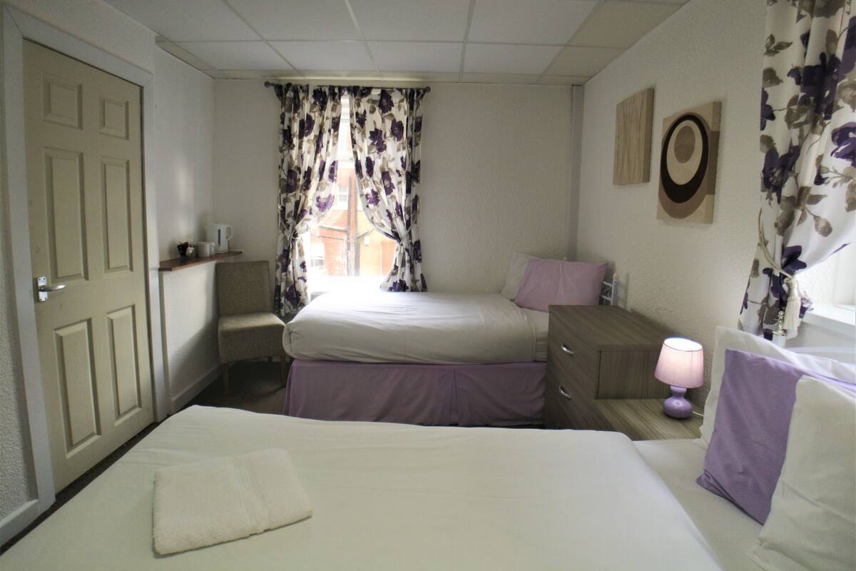 A bedroom with a bed, a chair, a nightstand, a lamp, and a window with floral curtains.