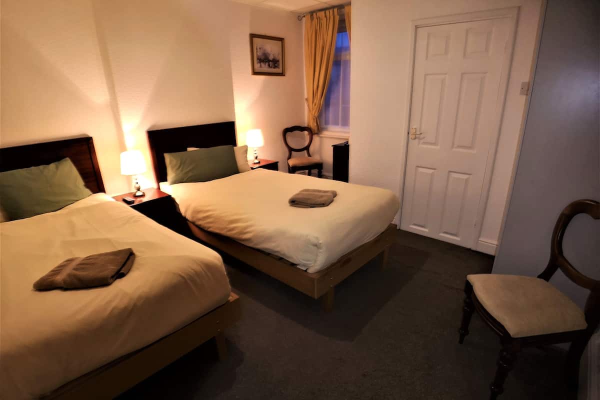 A hotel room with two beds, a chair, a nightstand with a lamp, a picture on the wall, and a door.