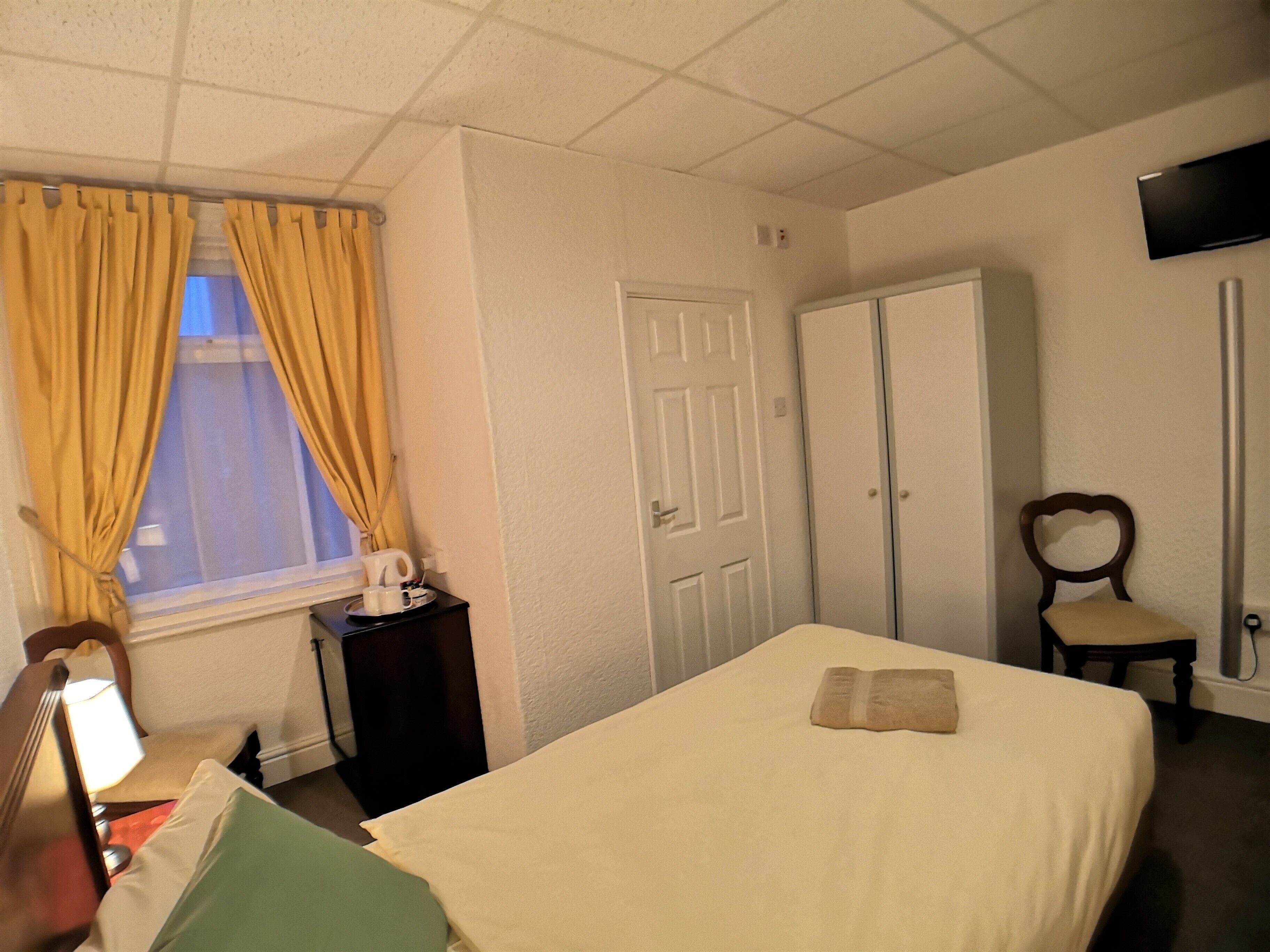 Una habitación de hotel con una cama, una silla, un escritorio con lámpara, un armario y un televisor en la pared.